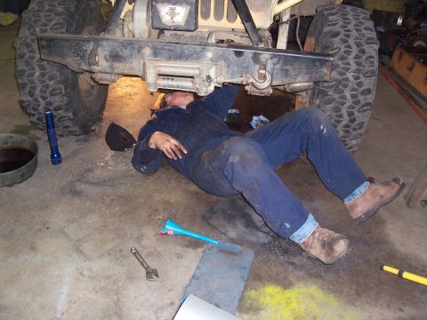 1988 Suzuki Samurai - A person is performing maintenance on the undercarriage of a vehicle, surrounded by tools and fluids.