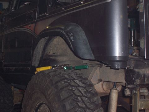 1988 Suzuki Samurai - Close-up view of the fender and tire of a dark-colored off-road vehicle, with tools resting on the tire.