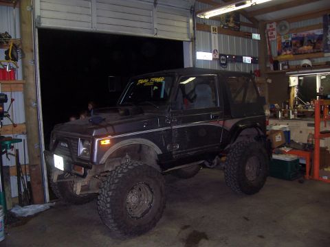 1988 Suzuki Samurai - This heavily modified off-road vehicle is parked inside a cluttered garage with the door open.