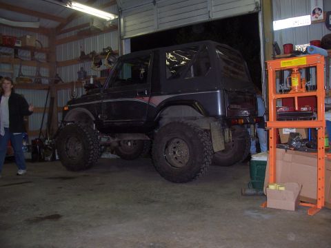 1988 Suzuki Samurai - A black Suzuki Samurai with a soft top and lifted suspension is parked inside a garage.