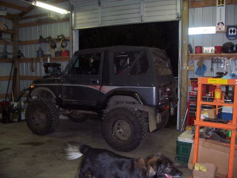 1988 Suzuki Samurai - An off-road vehicle with oversized tires sits inside a garage, modified with a roll cage visible through the windows.