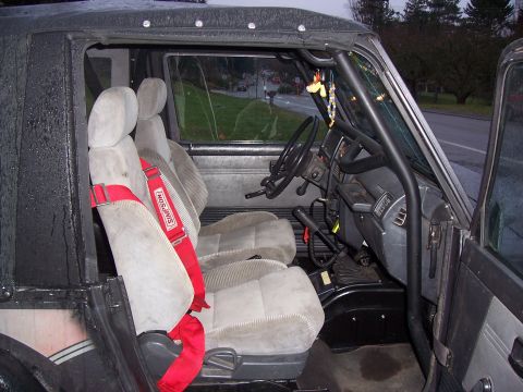 1988 Suzuki Samurai - The interior of a Suzuki Samurai features gray seats, a red Simpson racing harness, and a black roll cage.