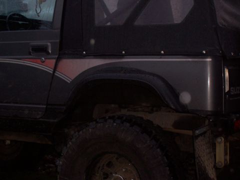 1988 Suzuki Samurai - A dark gray Suzuki Samurai is shown from the side, a soft top and a distinctive stripe on the rear fender.