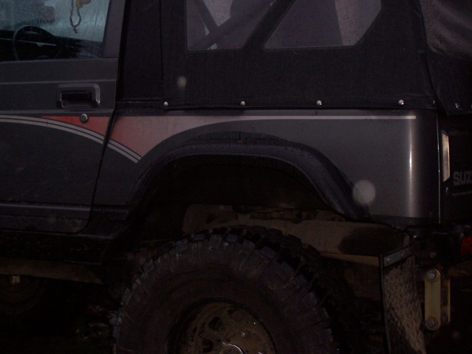 Dark gray Suzuki Samurai with red and silver stripe on the fender, soft top, and off-road tire