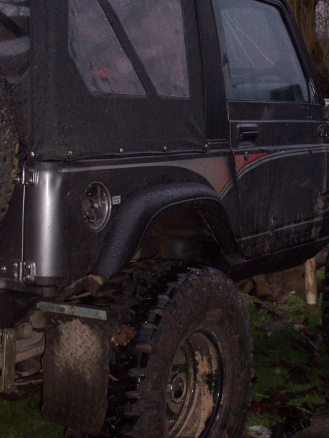 1988 Suzuki Samurai - This black soft-top SUV features large off-road tires and mud flaps, suggesting it is modified for off-road use.