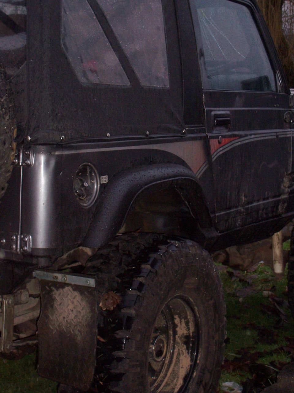 Side view of black soft-top SUV with large off-road tires and mud flaps