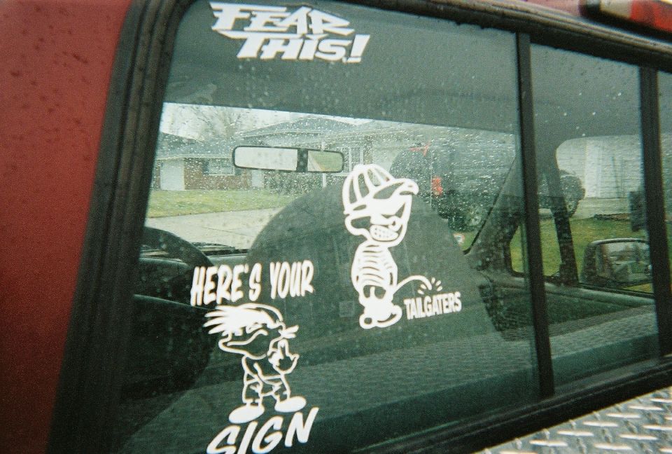 Pickup rear window with 'FEAR THIS!' and Calvin peeing decals reading SIGN and TAILGATERS
