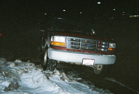 1996 Ford F-150 - A red Ford F-150 is partially stuck in snow at night, showing its front grille and headlights.