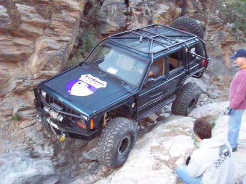 1994 Jeep Cherokee - A modified Jeep Cherokee navigates a rocky terrain, with two people observing the off-road vehicle.