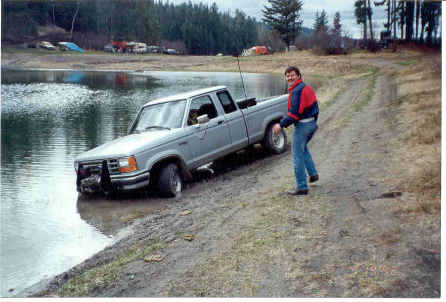 Silver Ford Ranger pickup truck stuck in water with a man standing nearby