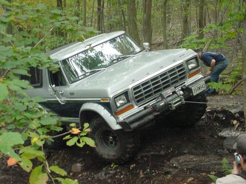 1978 Ford Bronco - A 1978 Ford Bronco is shown off-roading through a wooded area, utilizing its winch for assistance.