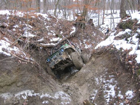 1992 Ford Bronco - Off-road vehicle struggling in a muddy, wooded terrain with snow patches.