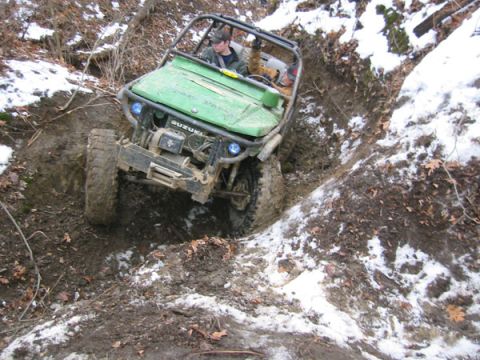 1992 Ford Bronco - A green off-road vehicle with a roll cage is shown traversing a challenging muddy and snowy terrain.