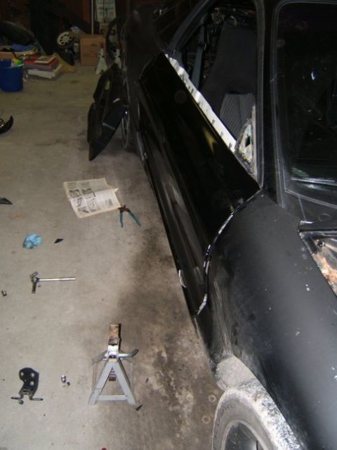 1993 Ford Probe - A black car is in a garage with its door removed, revealing the interior and some body damage.