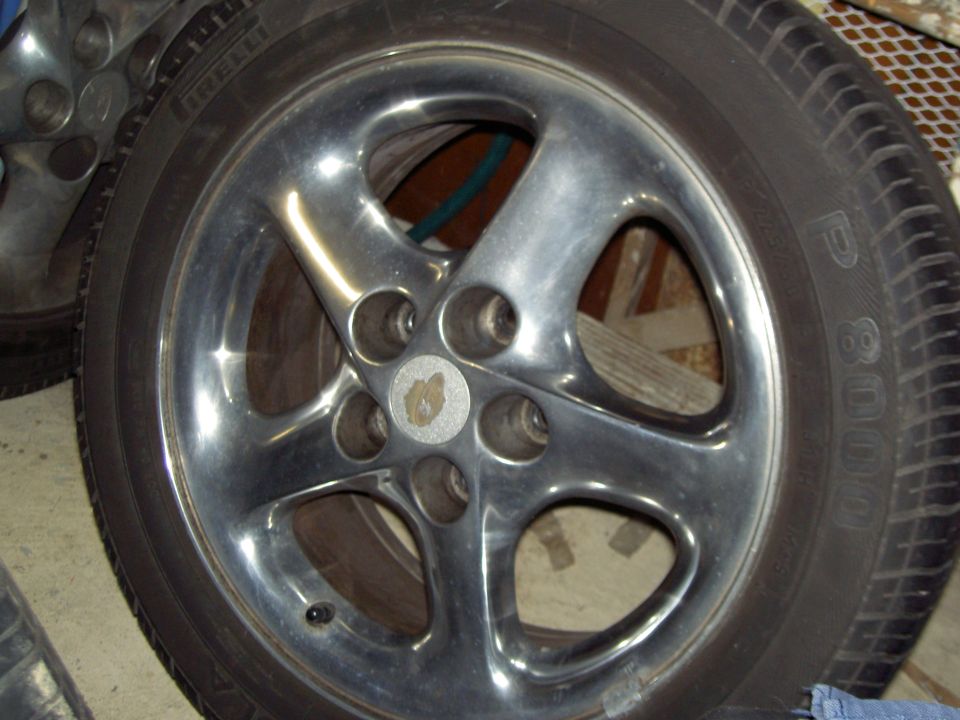 Dark five-spoke alloy wheel with Pirelli P8000 tire lying on a concrete floor