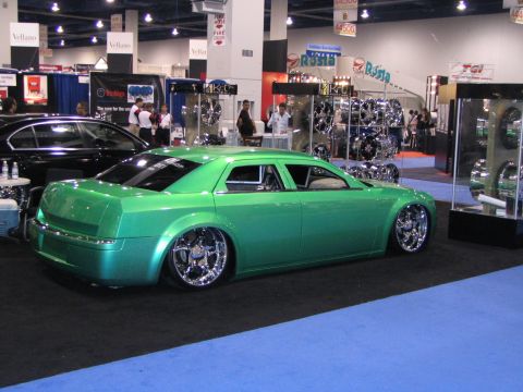 1986 Pontiac Fiero - A custom green sedan with large chrome wheels is displayed at an auto show.