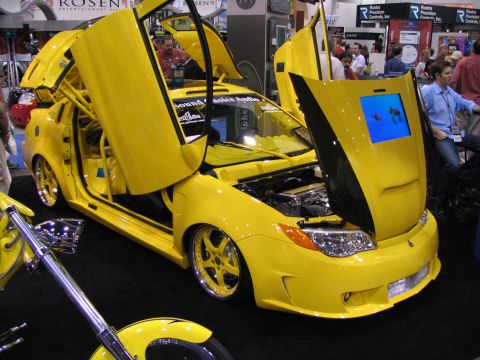 1986 Pontiac Fiero - Custom yellow car with unique doors and hood display at an auto show.