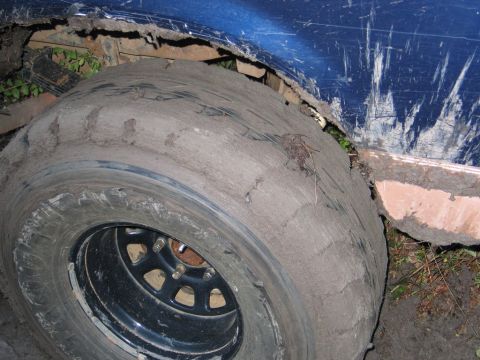 1995 Ford Bronco - A blue SUV's tire is deeply embedded in mud, with the fender showing significant wear and tear.