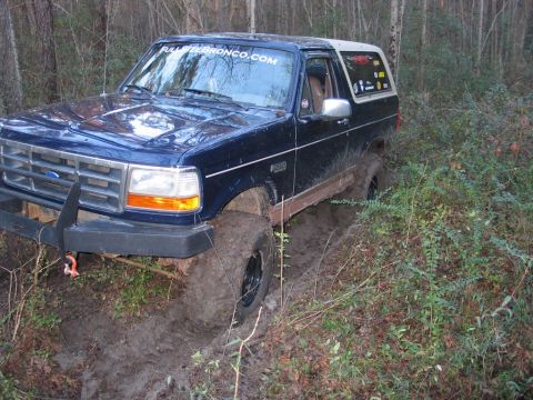 1995 Ford Bronco - This blue 1995 Ford Bronco is stuck deep in the mud, with its front tire submerged and the body resting on the embankment.