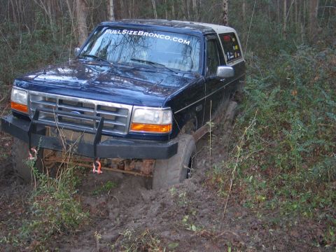 1995 Ford Bronco - A blue Ford Bronco is stuck in thick mud, surrounded by trees and brush.