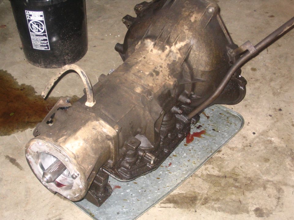 Dirty transmission case removed and set on a galvanized sheet on garage floor, input shaft splines visible