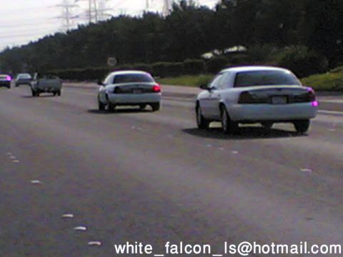 1999 Mercury Grand Marquis - A white police car is seen from behind on a highway with other vehicles.