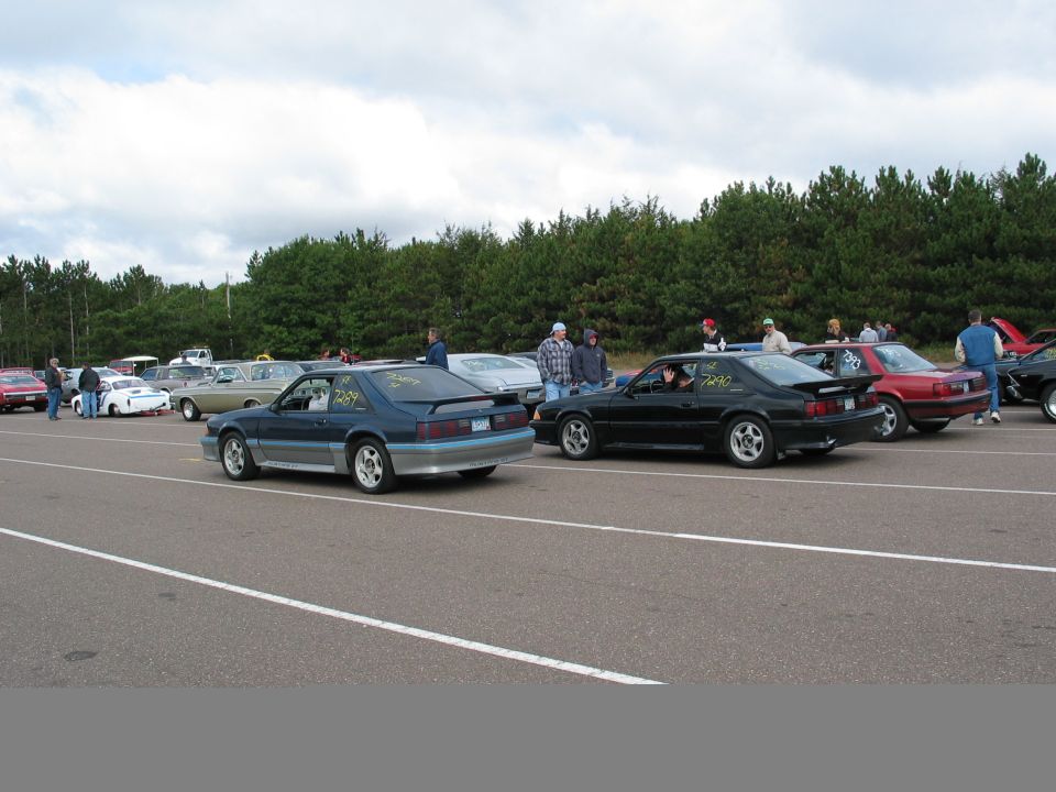 Blue and black 1990 Ford Mustangs on a racetrack, side-by-side