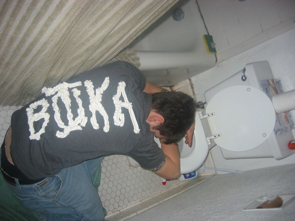 Person in jeans and a grey t-shirt with white lettering leans over a toilet