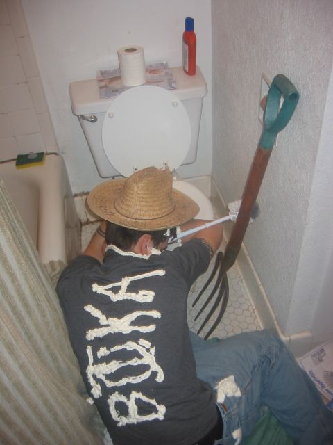 1989 Ford Bronco - A person wearing a straw hat and a shirt with white lettering appears to be working on a toilet in a bathroom.