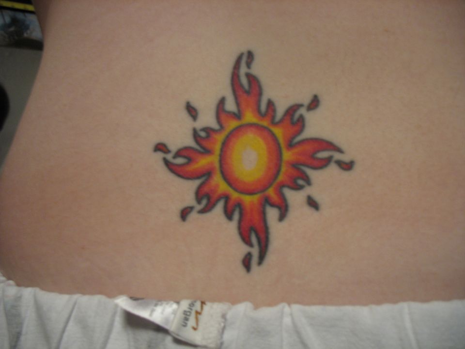Sun-and-flames tattoo on lower back skin above waistband of pants