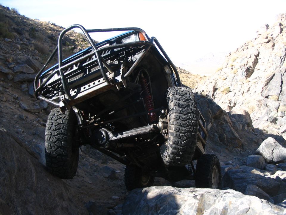 Front view of lifted truck on a steep rock ledge with tube bumper, shocks and big mud tires