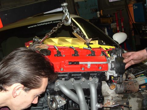 1996 Ford Probe - Mechanics work on an engine being removed from a vehicle in a garage.