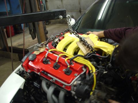 1996 Ford Probe - Engine removal in progress, showing the red valve cover and yellow intake manifold, with a chain hoist attached.