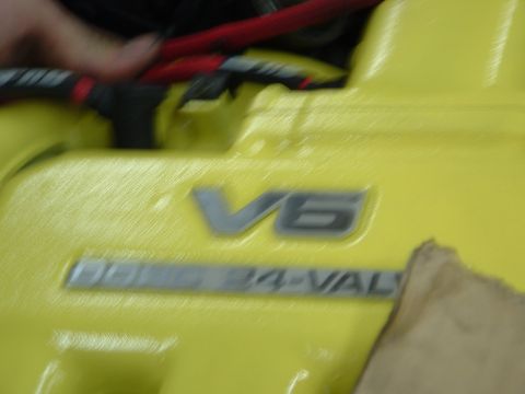 1996 Ford Probe - Close-up of a yellow engine valve cover with V6 and 24-VAL markings, indicating a 24-valve V6 engine.