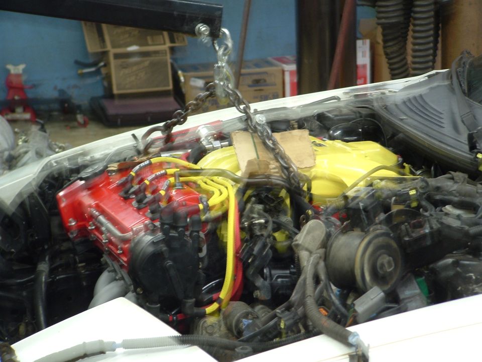 engine bay with engine hoist attached, red and yellow engine components visible