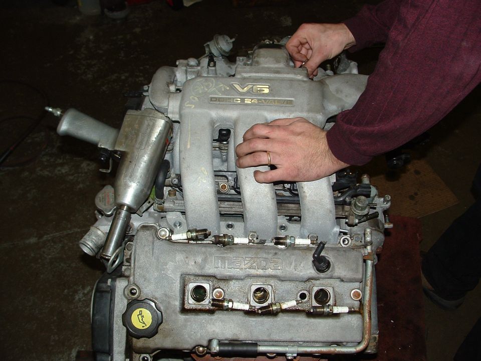 Mazda V6 engine with "24 VALVE" text, being worked on by hands