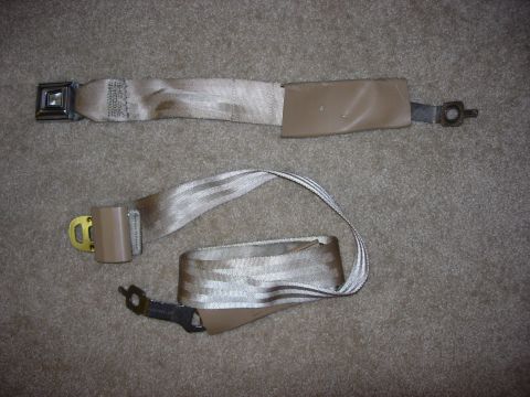 1998 Ford Crown Victoria - Two tan seat belts are shown laid out on a carpeted surface. One belt has a metal buckle and a plastic guide, while the other is partially…