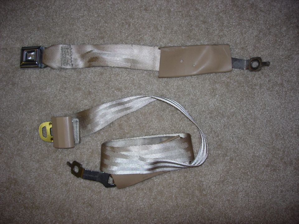 Disassembled tan and beige automotive seat belts laid out on carpet