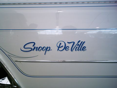 1986 Ford Bronco - Close-up of a white car's body panel lettered "Snoop DeVille" in blue script, framed by hand-painted blue pinstriping and a chrome body-sid…