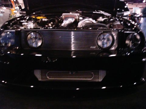 1986 Ford Bronco - The front of a black car is shown with its hood open, revealing the engine and custom modifications.