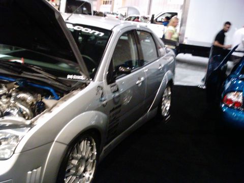 1986 Ford Bronco - A modified silver sedan is displayed with its hood open, revealing a custom engine bay.