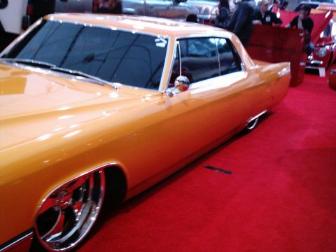 1986 Ford Bronco - This custom orange coupe features large chrome wheels and tinted windows, displayed indoors on a red carpet.