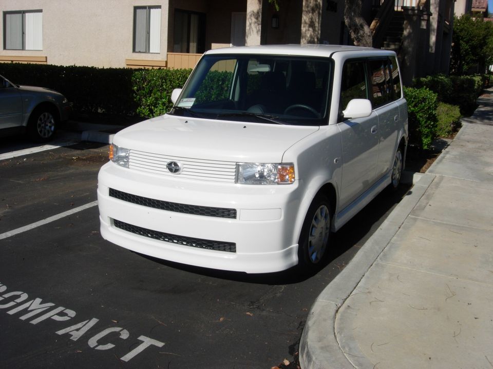 White Scion xB with front lip spoiler parked in a compact stall, front three-quarter
