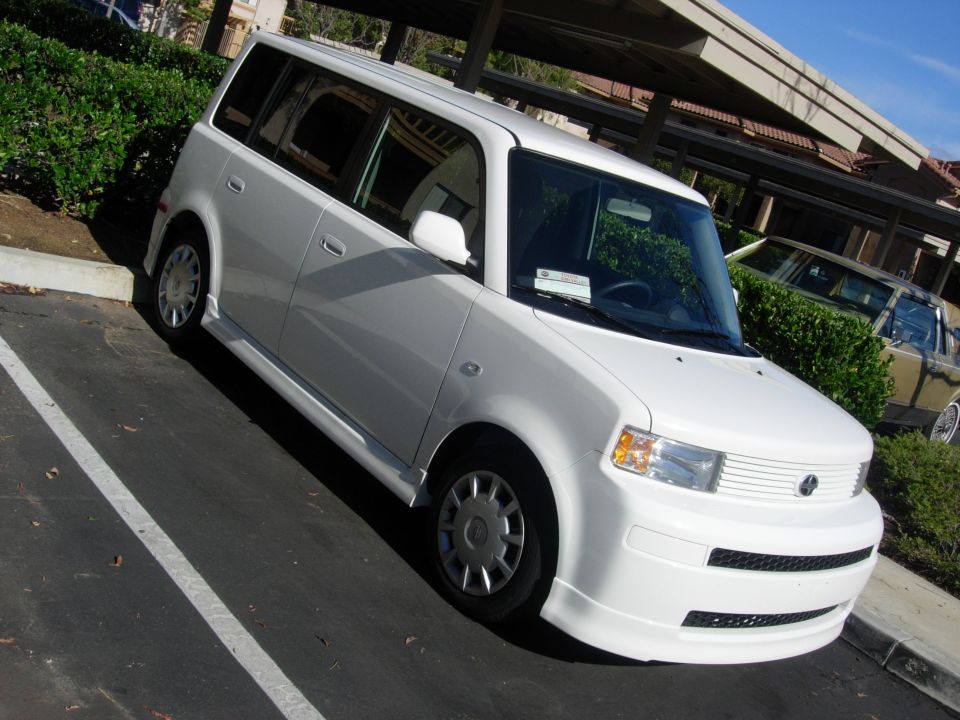 White first-gen Scion xB box wagon parked beside a hedge in a parking lot