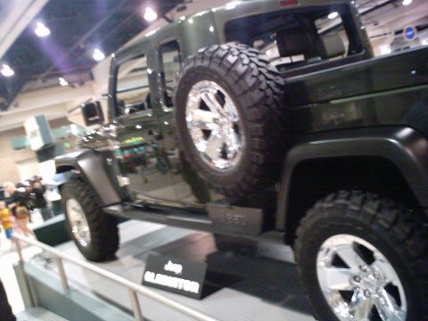 1986 Ford Bronco - A dark green Jeep Gladiator is displayed with its spare tire prominently mounted on the rear.