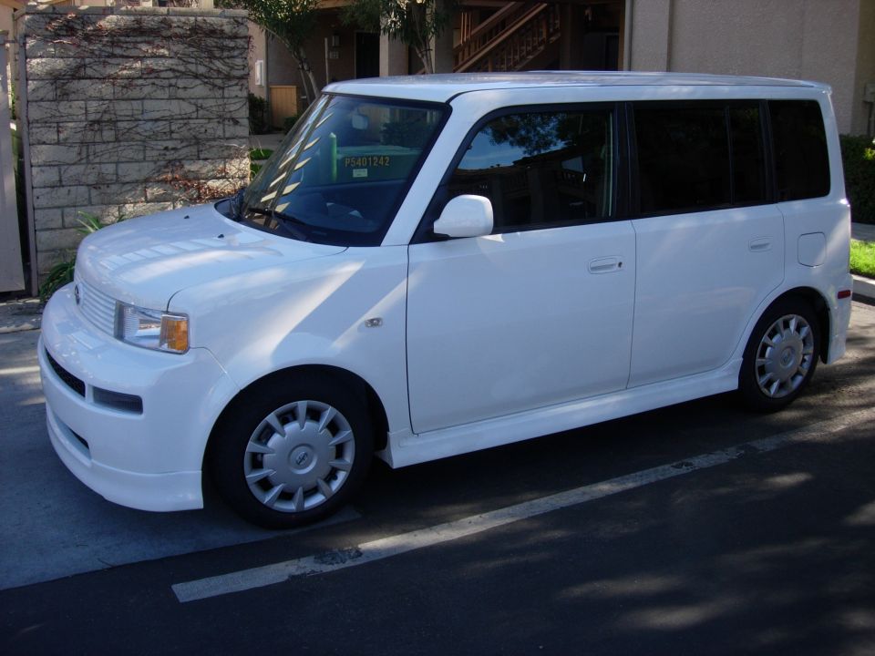 White boxy Scion xB parked, driver-side 3q-front view with visible windshield tag.