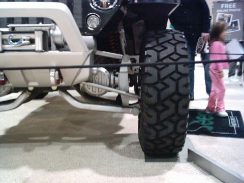 1986 Ford Bronco - Close-up view of an off-road vehicle's front suspension, large tire, and winch, with a child in the background.