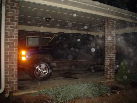 1984 Ford Bronco - This dark pickup truck is parked under a carport, with its front turn signal on.