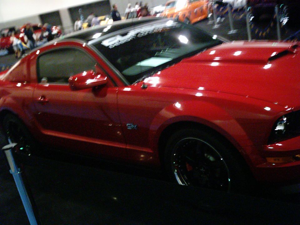 Red coupe with black roof and hood scoop, side view. Black rims and tinted windows