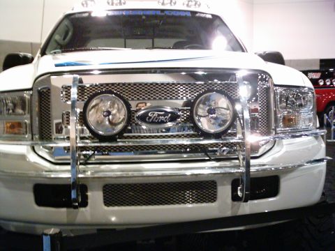 1986 Ford Bronco - Frontal view of a white Ford truck a prominent chrome grille and a bull bar with auxiliary lights.